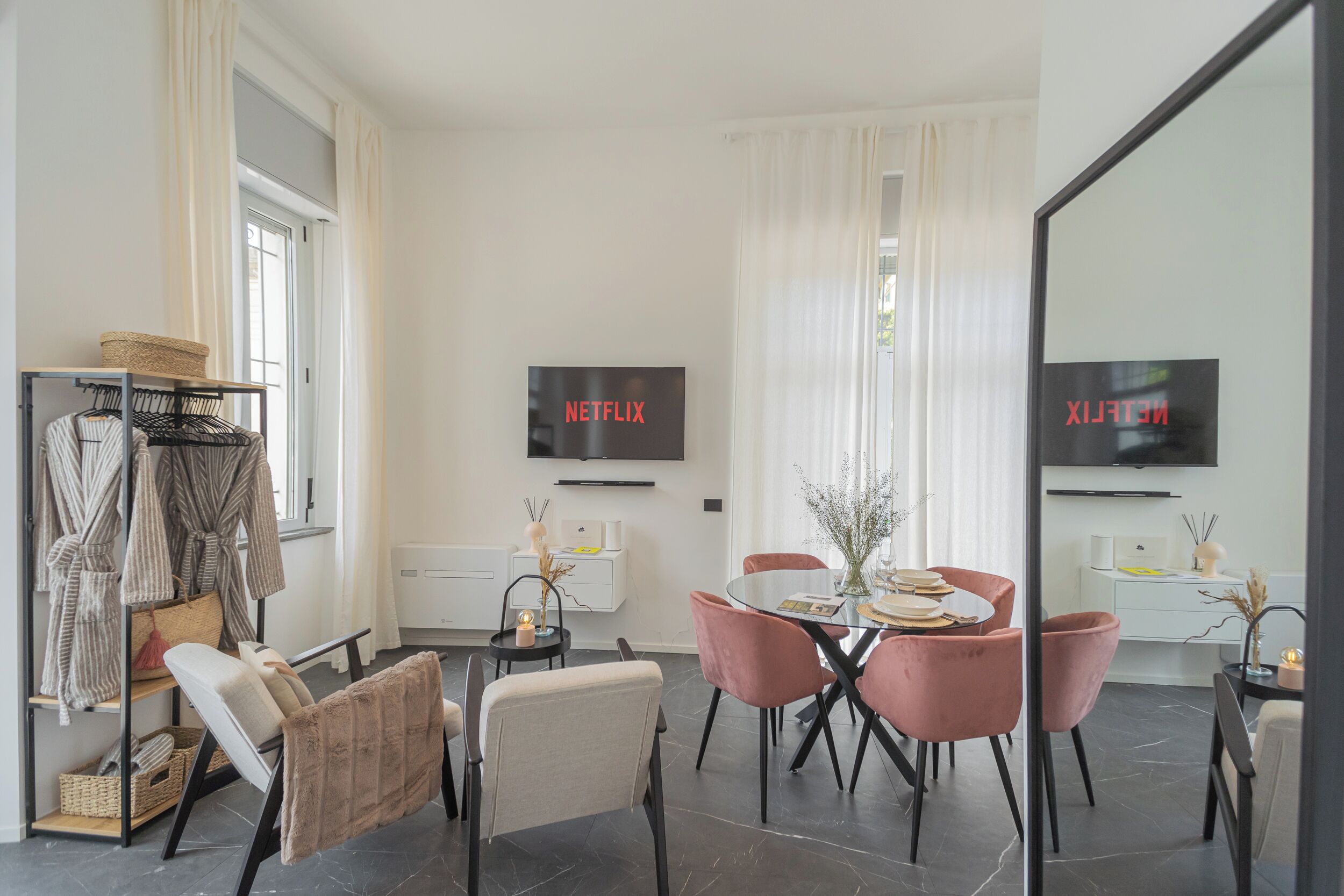 A modern living room with a dining area, a TV mounted on the wall, and a large mirror reflecting the room.