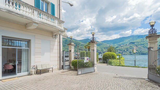 A building with a balcony, a gate, and a view of a lake and mountains. - Piccola Como Lotus by Rent all Como (Carate Urio)