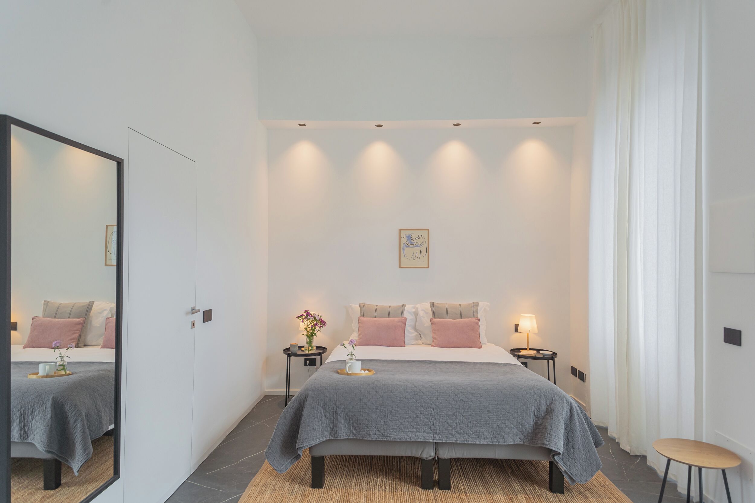 Une chambre moderne avec un grand lit, des tables de chevet, un miroir et une œuvre d’art accrochée au mur.