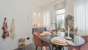 A dining area with a round glass table, pink chairs, and a bed in the background. - Piccola Como Lotus by Rent all Como (Carate Urio)