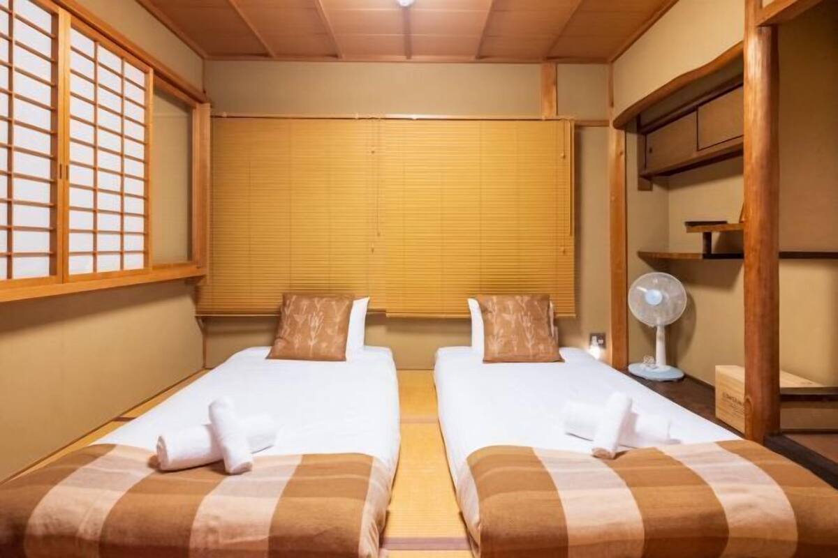 Ein Zimmer mit zwei Betten, einem Ventilator und einem Fenster mit Holzjalousien.