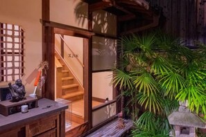 En traditionell japansk interiör med en trätrappa, en receptionsdisk och frodiga, gröna växter.