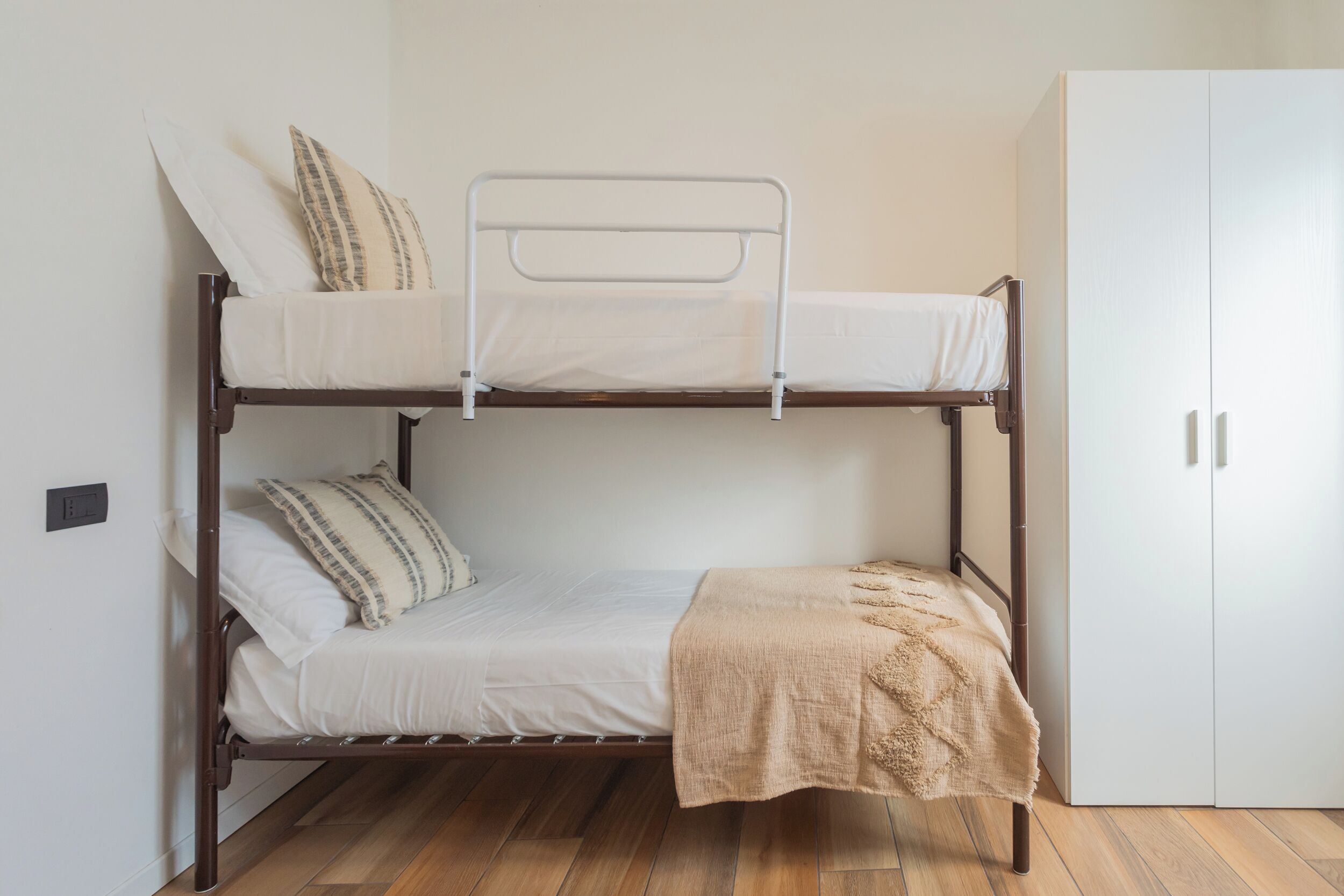 Una cama litera con una cama inferior, un armario blanco y suelo de madera.