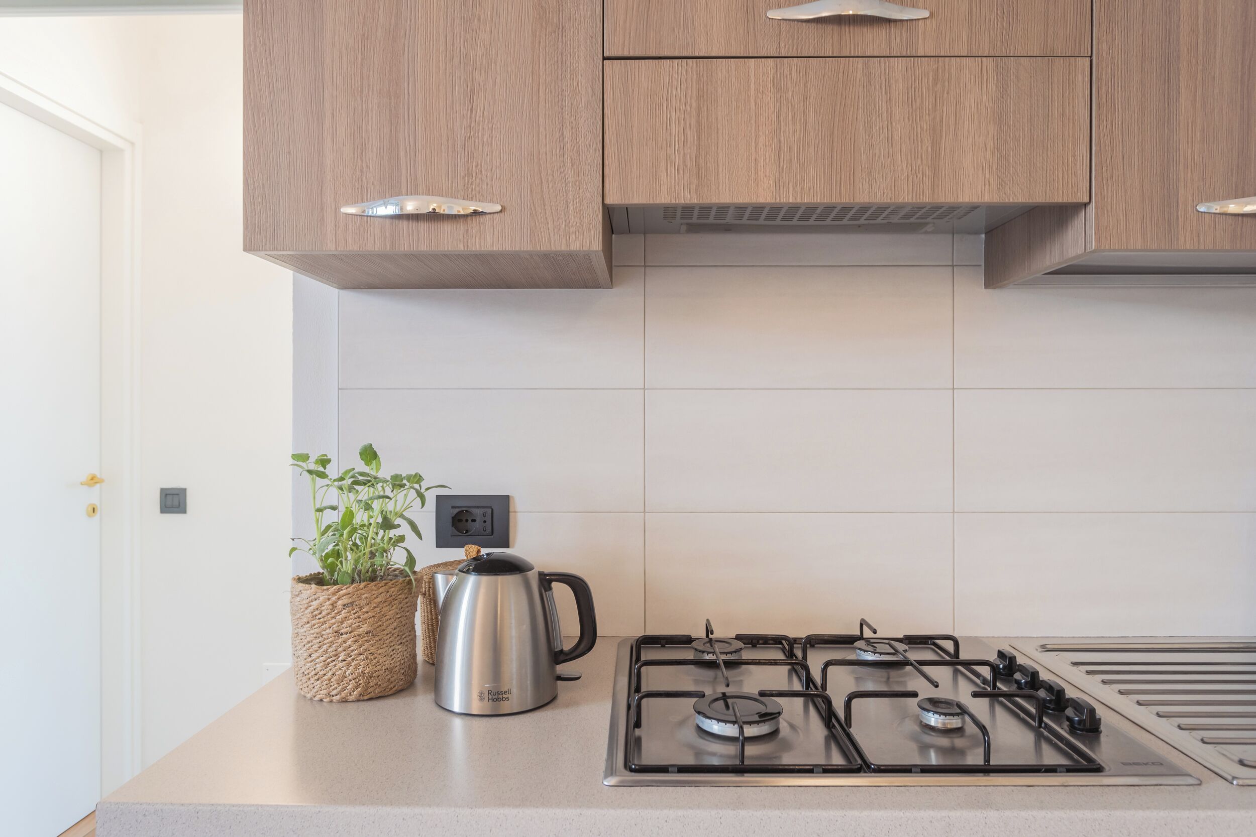 Une cuisine moderne avec des meubles en bois, une cuisinière à gaz et une bouilloire posée sur le plan de travail.