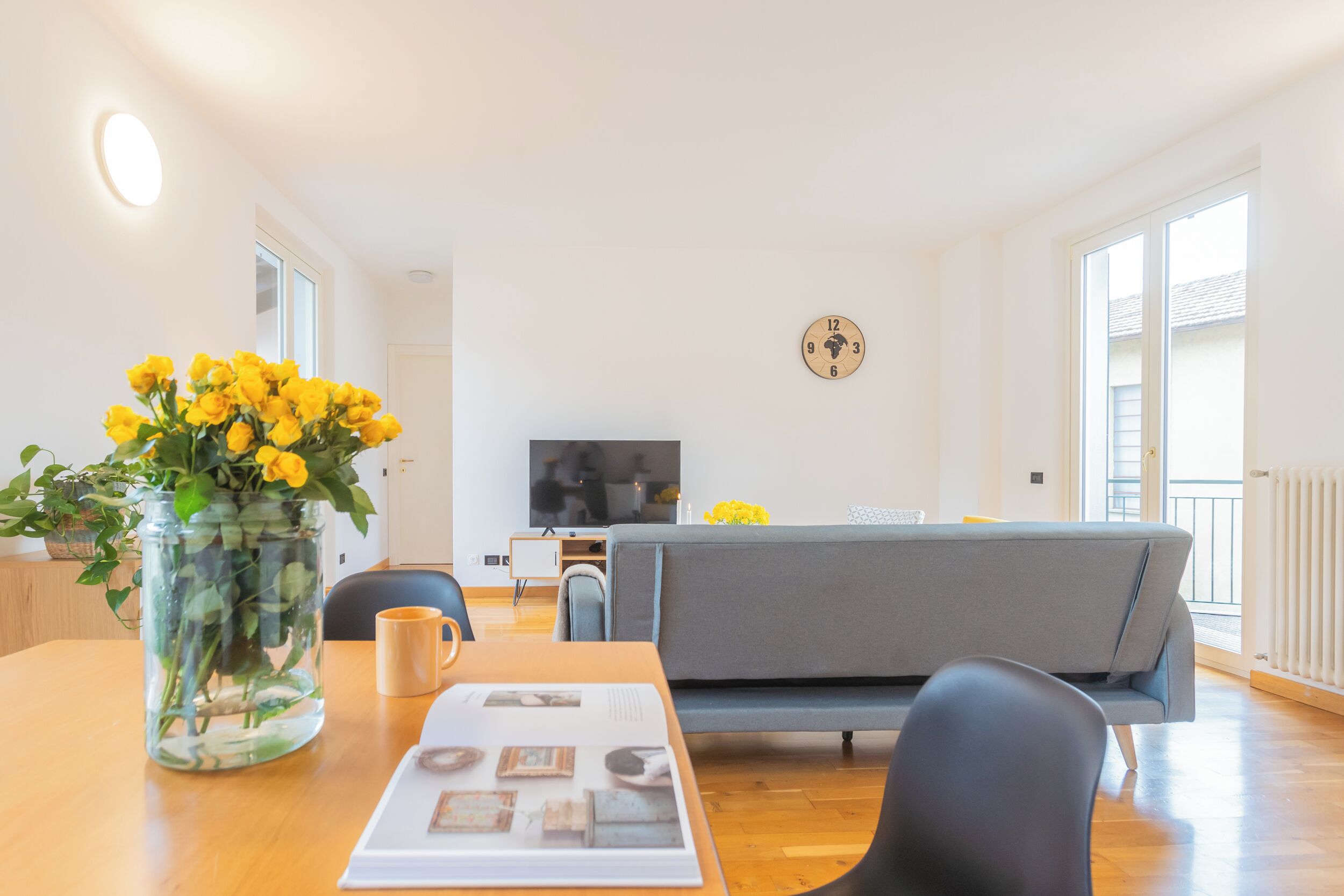 A modern living room with a sofa, a coffee table, and a TV. There is a vase with yellow flowers on the table.