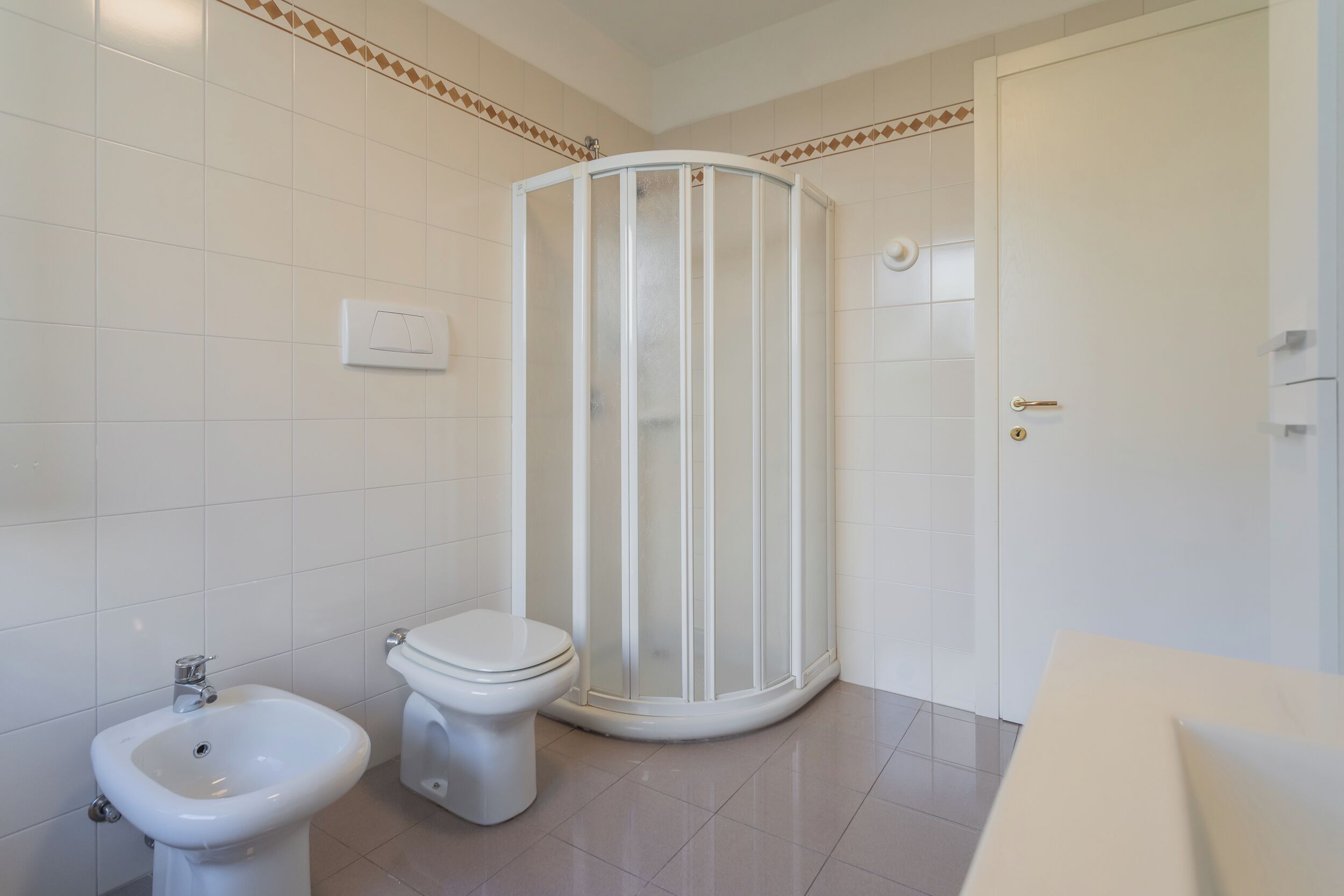 Un baño con cabina de ducha, inodoro, bidé y una puerta con pomo dorado.