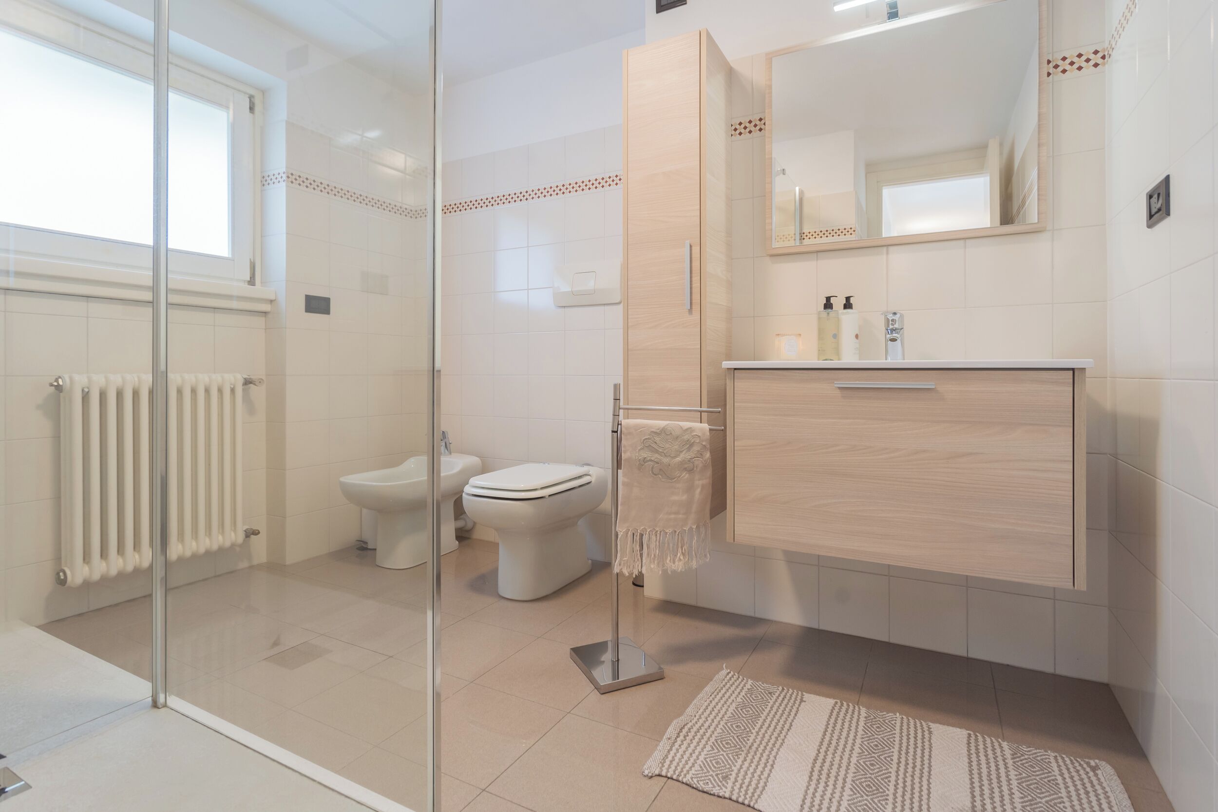 Une salle de bain moderne avec une douche à l’italienne en verre, des toilettes, un lavabo avec un miroir et un radiateur.