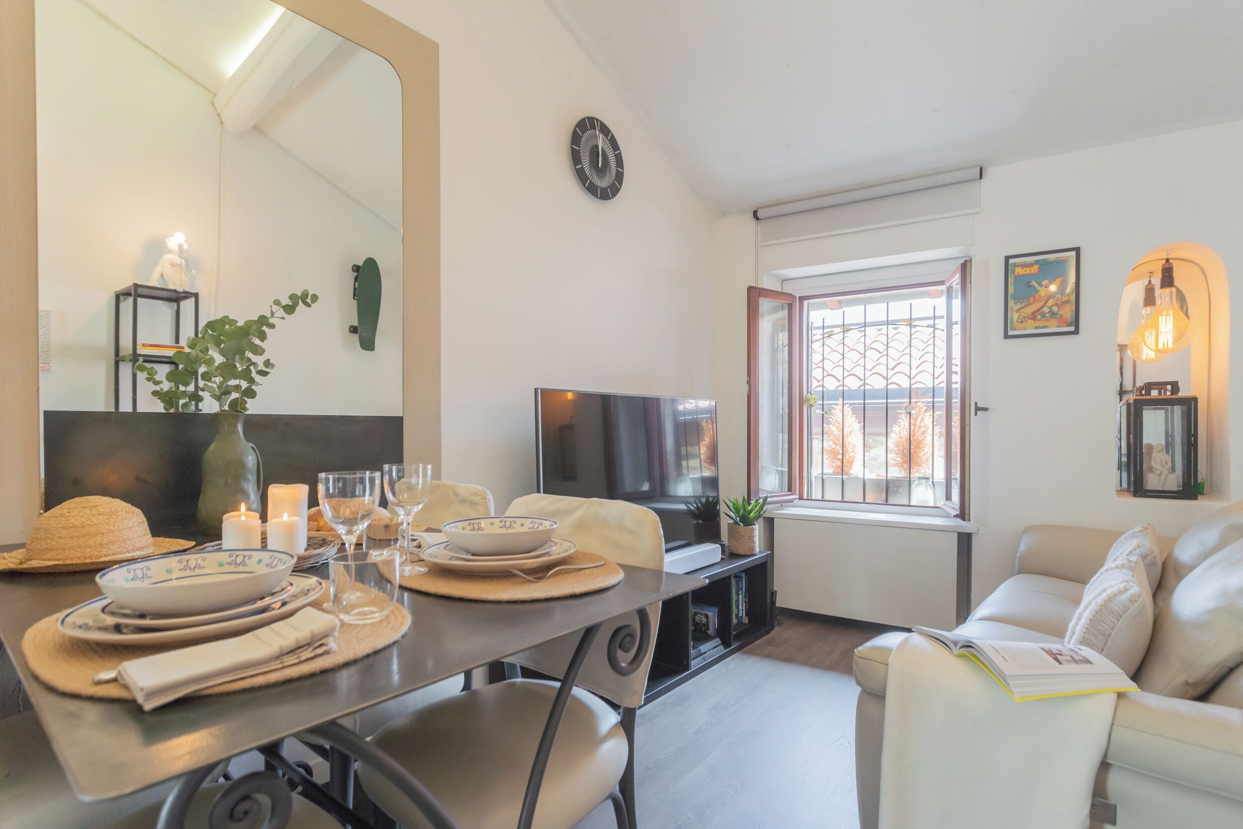A modern living room with a dining table set for four, a sofa, a TV, and a window with a view.