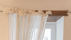 Una habitación con ventana, cortina, una mesita, una vela y una planta.