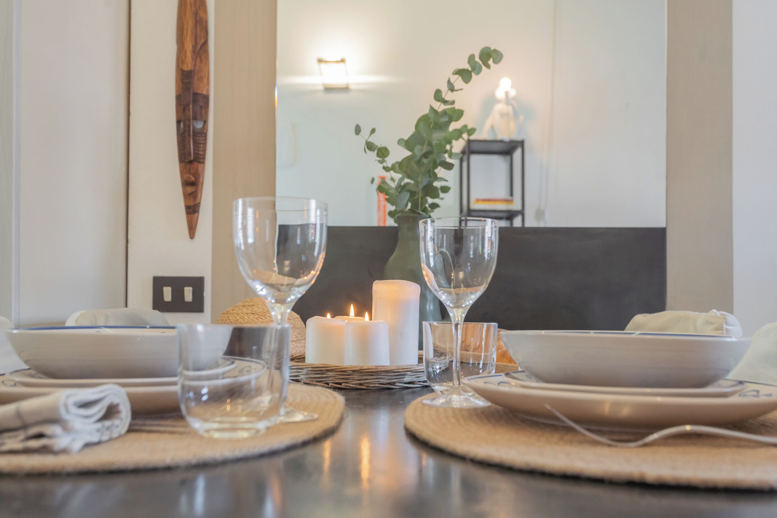 Una mesa de comedor dispuesta con cristalería transparente, platos blancos y un centro de mesa con una vela encendida.