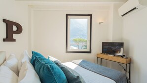 Ein Schlafzimmer mit Bett, Kissen, Fernseher und Fenster mit Blick auf die Berge.