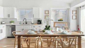 A modern kitchen with white cabinets, a wooden dining table set for four, and a kitchen island with a coffee machine.