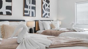 A hotel room with two beds, a bedside table with a lamp, and abstract wall art.