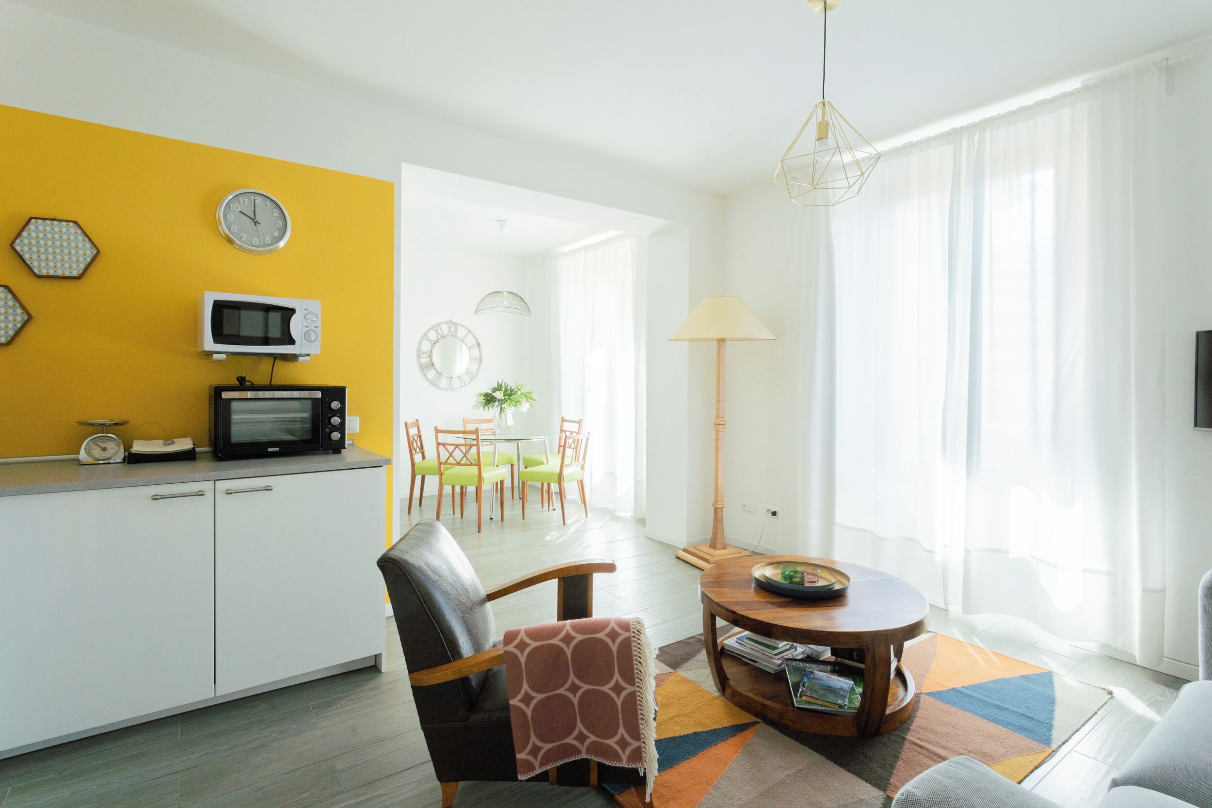 A modern living room with a dining area, a kitchen with retro appliances, and a bright yellow accent wall.