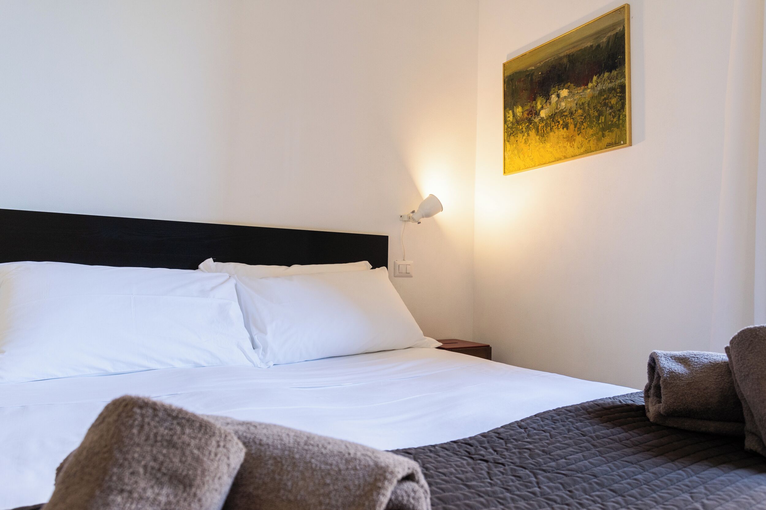 A neatly made bed with white linens, a dark headboard, and a painting on the wall.