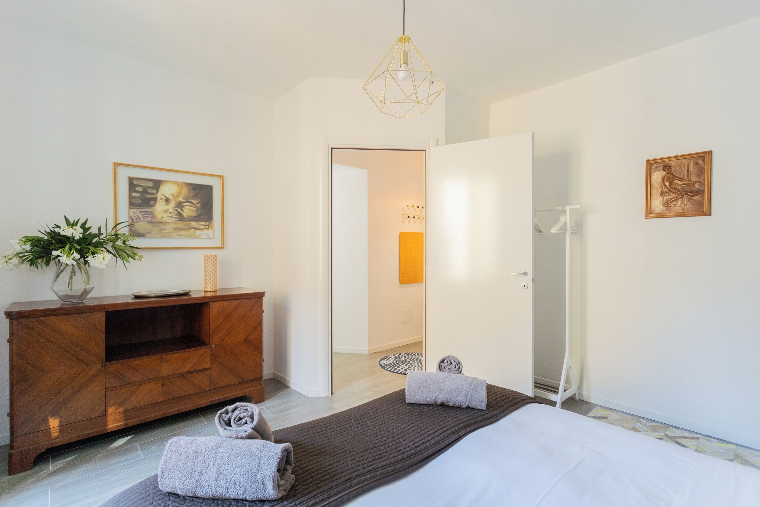Ein modernes Hotelzimmer mit einem Bett, einer Holzkommode, einem Spiegel und einer Tür zu einem Badezimmer.