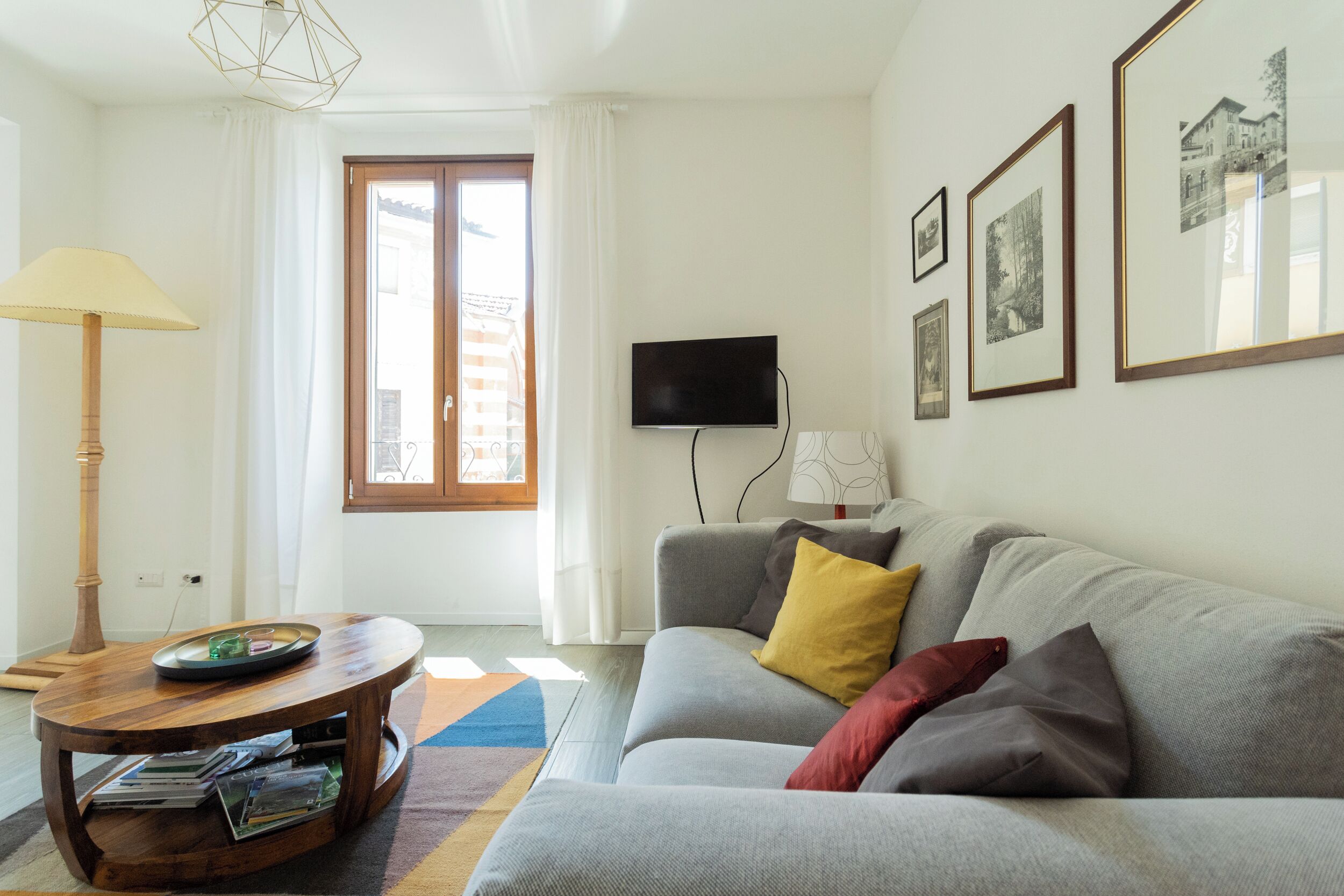 A living room with a grey sofa, a wooden coffee table, a flat-screen TV, and framed pictures on the wall.