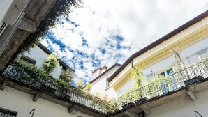 Une cour d’où l’on peut admirer le ciel, un balcon doté d’une balustrade et un bâtiment à la façade blanche et aux fenêtres en arc de cercle.