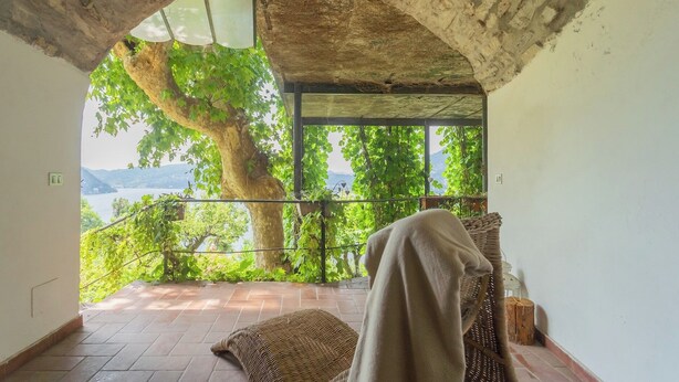 Un balcon avec vue sur un lac et des montagnes, une chaise en osier et une couverture.