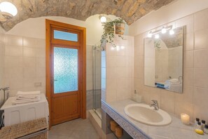 Un baño con puerta de madera, cabina de ducha de vidrio, lavabo con espejo y una pila de toallas.