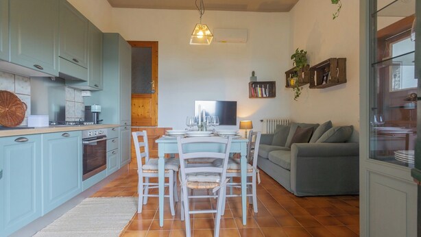 A compact kitchen with light blue cabinets, a dining area with white chairs, and a grey sofa in a living area. - Simon's Apartment With Amazing View by Rent all Como (Blevio)