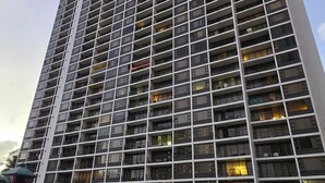 Un immeuble de grande hauteur doté d’une série de balcons, une aire de jeux avec un toboggan et une pelouse verdoyante.