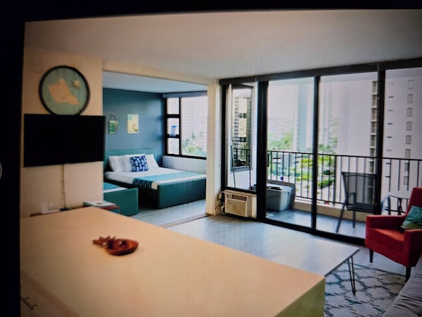 A modern bedroom with a large bed, a desk, and a balcony with a view of the city.