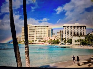 A beachside view with palm trees, a rainbow, and high-rise buildings in the background.