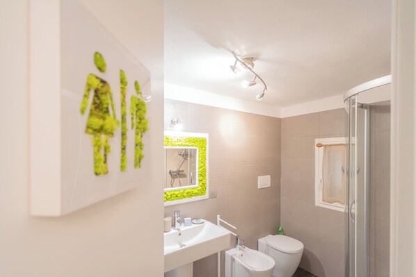 Uma casa de banho moderna com duche, sanita, lavatório e um espelho com parede vegetal verde.