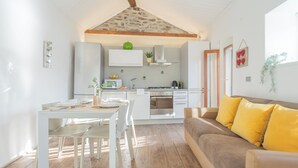 Una cocina compacta con armarios blancos, una isla central y un comedor con mesa y sillas blancas.