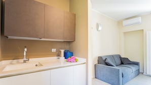 Een moderne keuken met witte kastjes, een spoelbak en een grijze bank in de woonkamer.