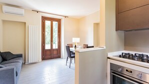 Een moderne keuken met een gasfornuis, een eethoek met een tafel en stoelen, en een grijze bank.