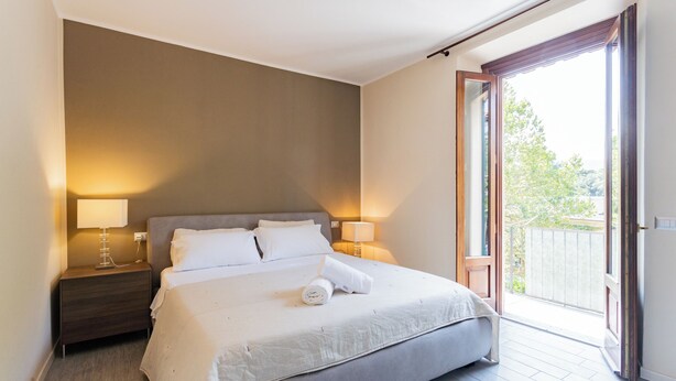 Een moderne slaapkamer met een groot bed, twee bedlampen, een houten nachtkastje en een schuifdeur naar een balkon.