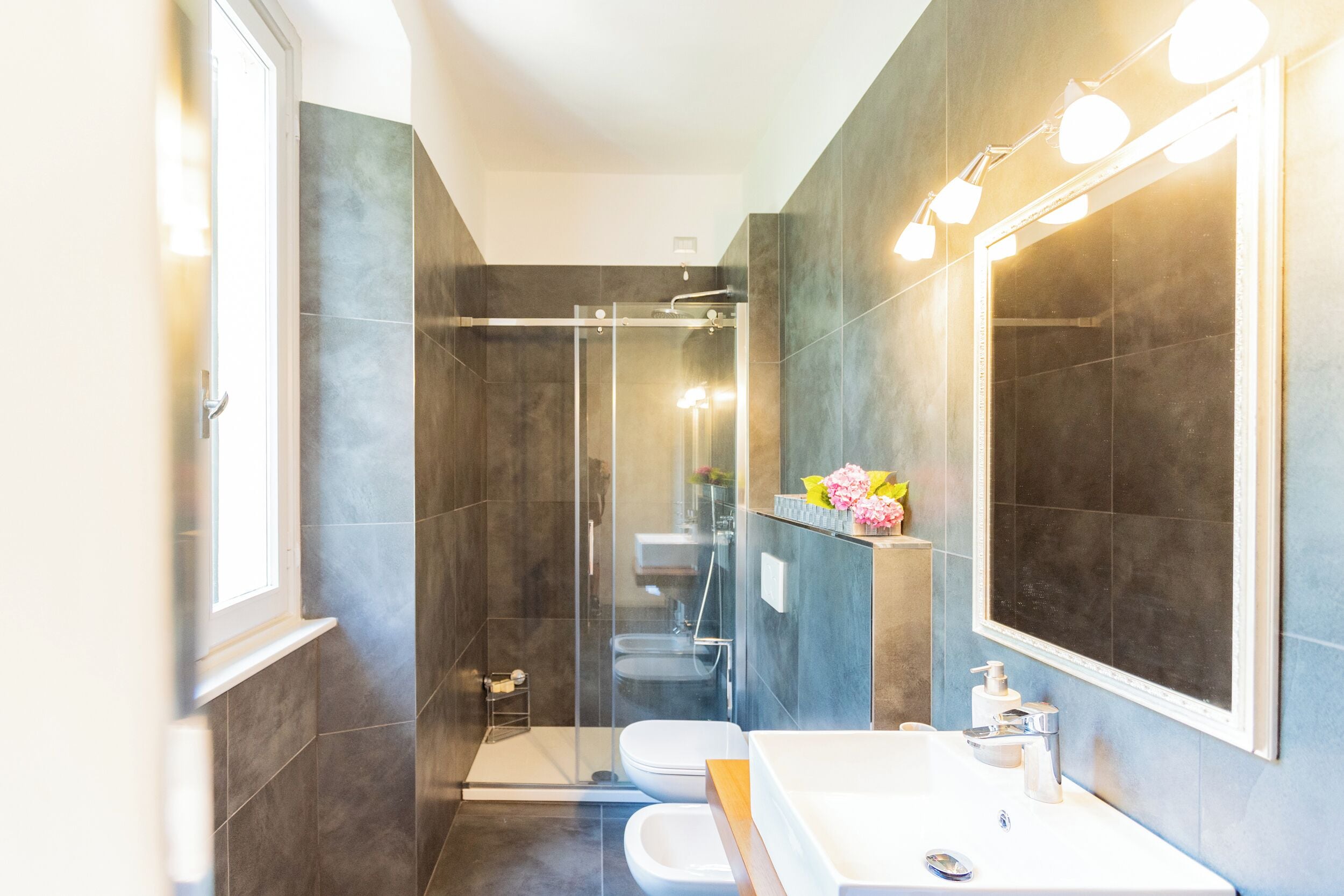 A modern bathroom with a glass-enclosed shower, a white sink, and a large mirror.