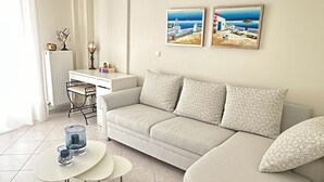 Una sala moderna con un sofá color beige, dos almohadones estampados, una pequeña mesa de centro blanca y dos cuadros colgantes con escenas costeras.