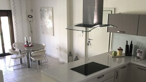Una cocina moderna con una isla central, electrodomésticos de acero inoxidable y un comedor con una mesa y sillas blancas.