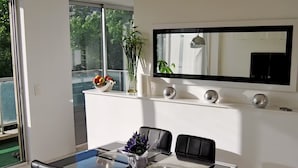 Et moderne spiseområde med et glasbord, sorte stole og en hvid bordplade med et spejl over.