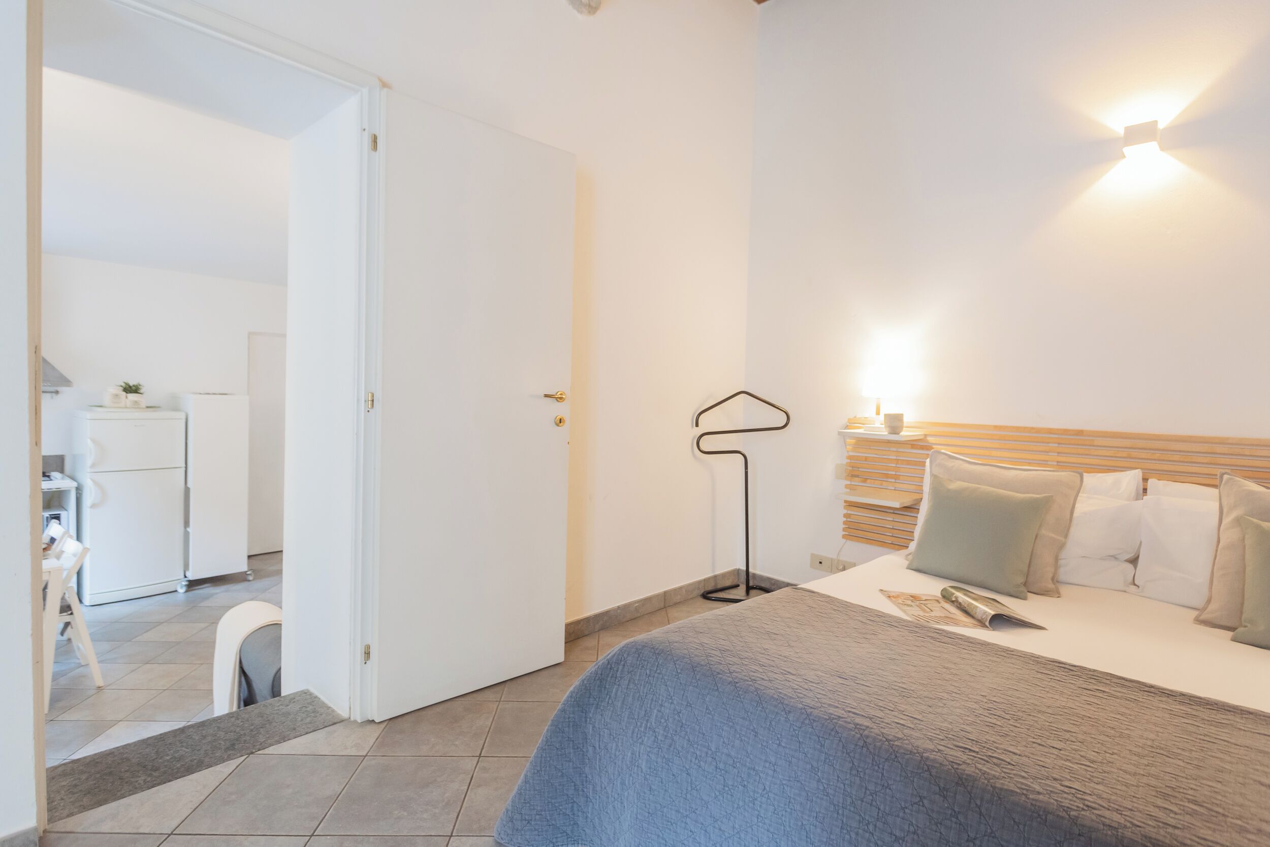 Et soveværelse med seng, natbord, lampe samt udsigt til køkken og spiseområde.