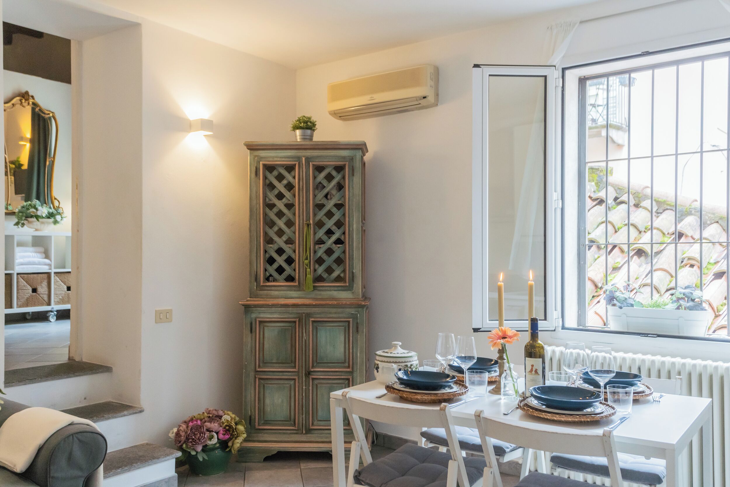 A dining area with a table set for four, a green cabinet, and a window with a view of the outside.