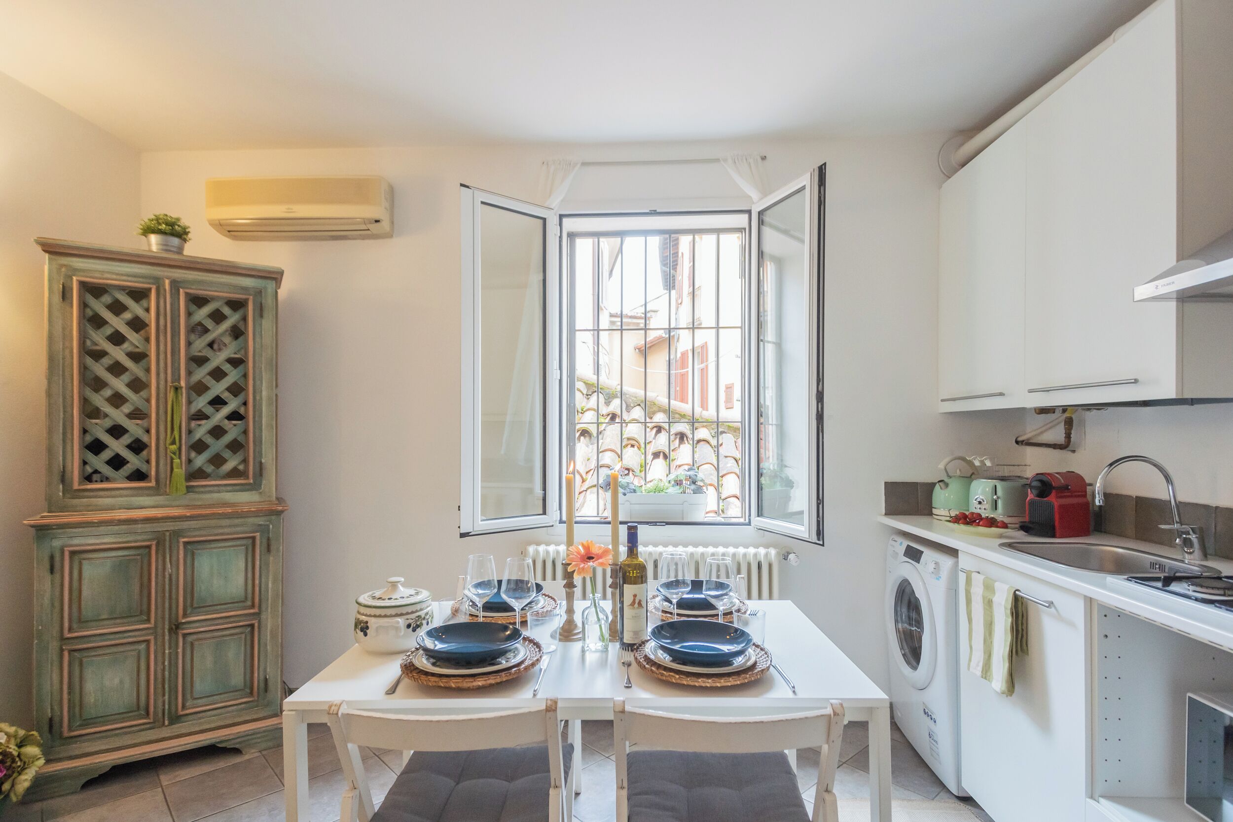 A compact kitchen with a dining area, a washing machine, and a window with a view of buildings.