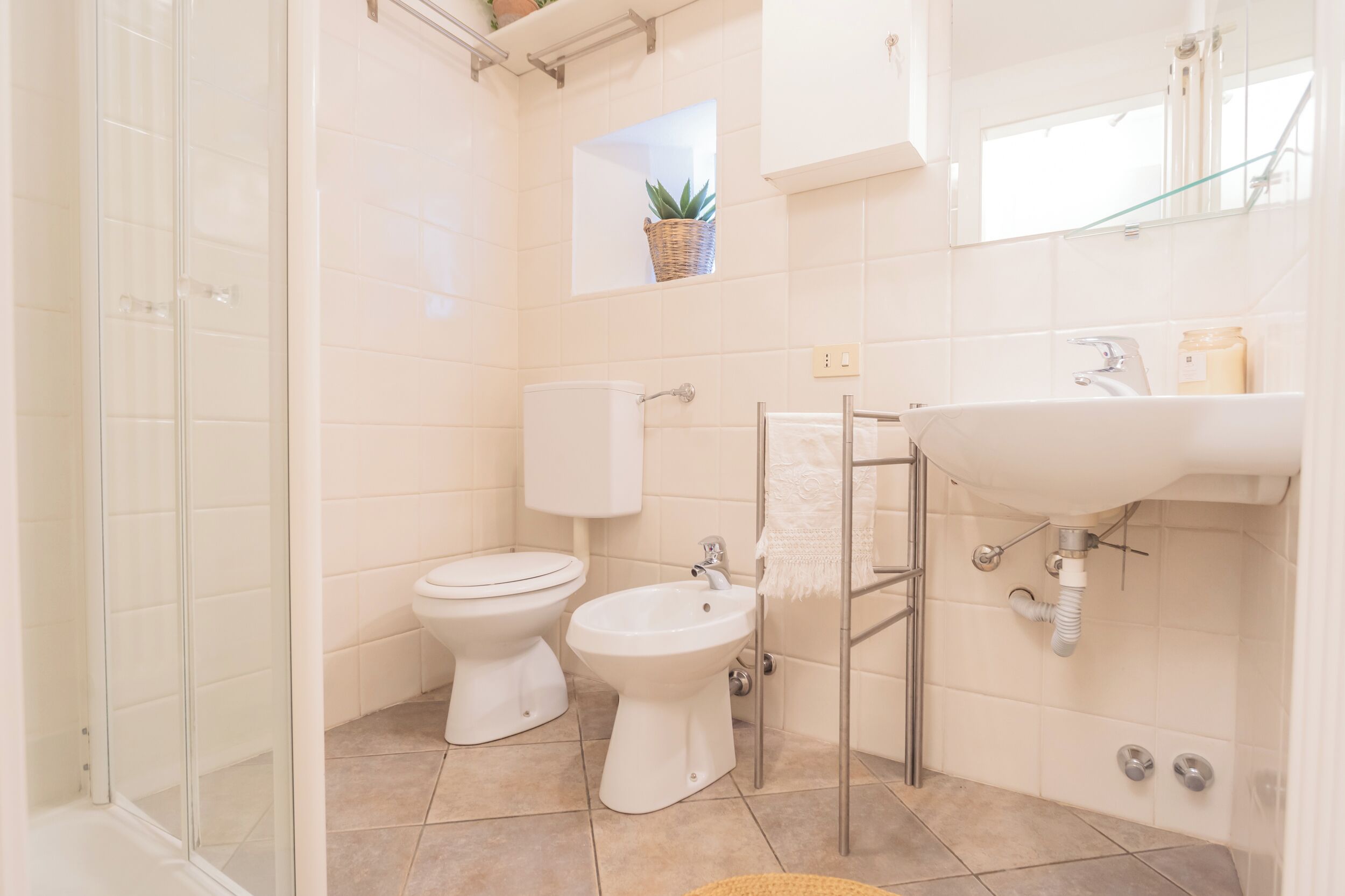 A bathroom with a glass shower enclosure, a toilet, a bidet, and a sink with a towel rack.