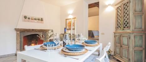 A dining area with a white table set for four, surrounded by white chairs. A wooden cabinet with glass doors is to the right.