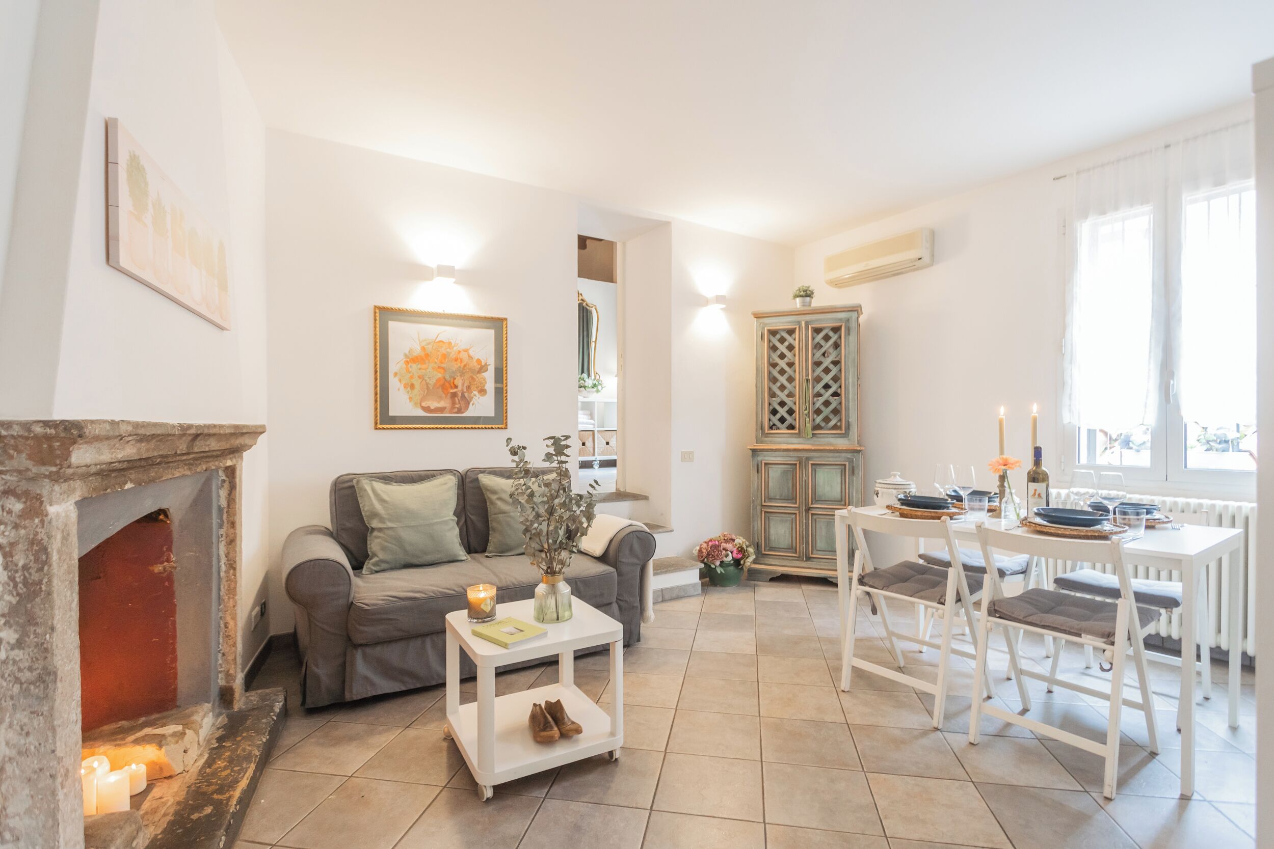 A living room with a fireplace, a sofa, a dining table with chairs, and a kitchen area with a cabinet.