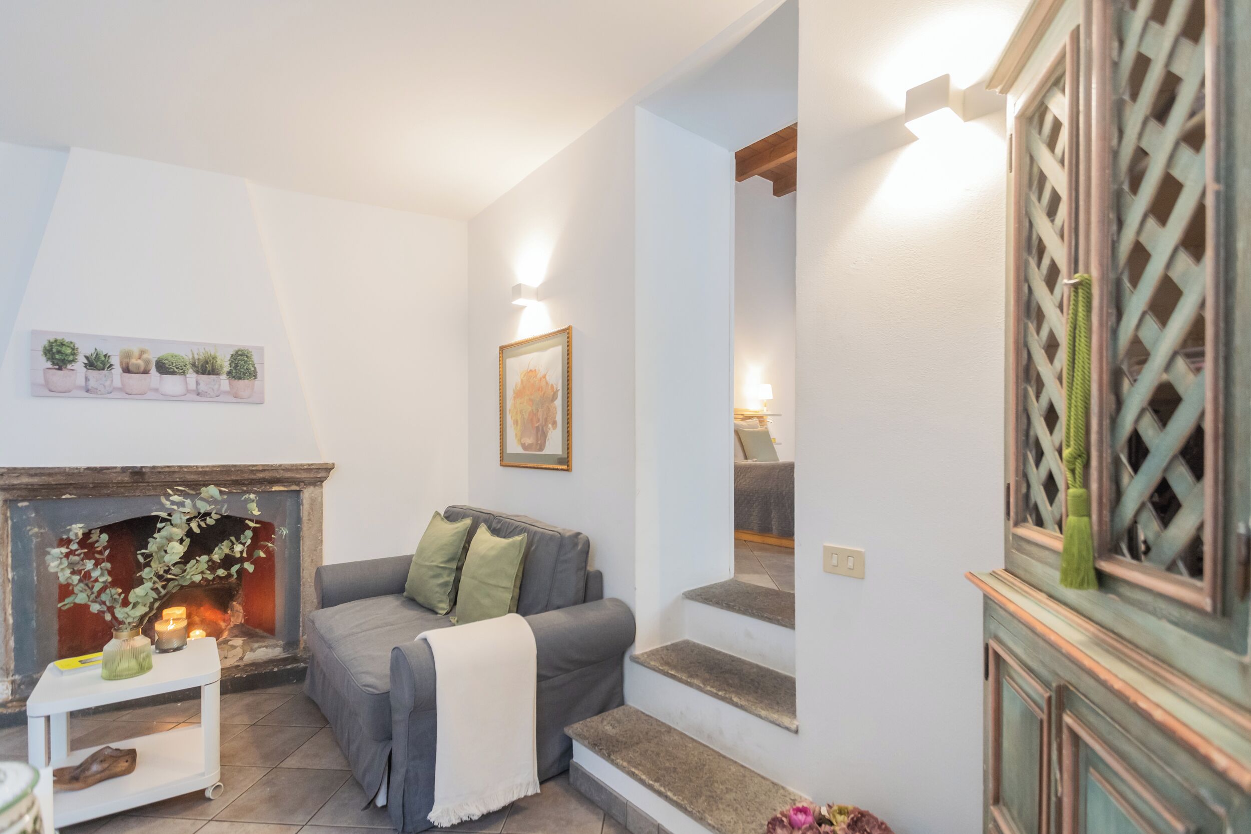 A living room with a fireplace, a sofa, a small table with candles, and a staircase.