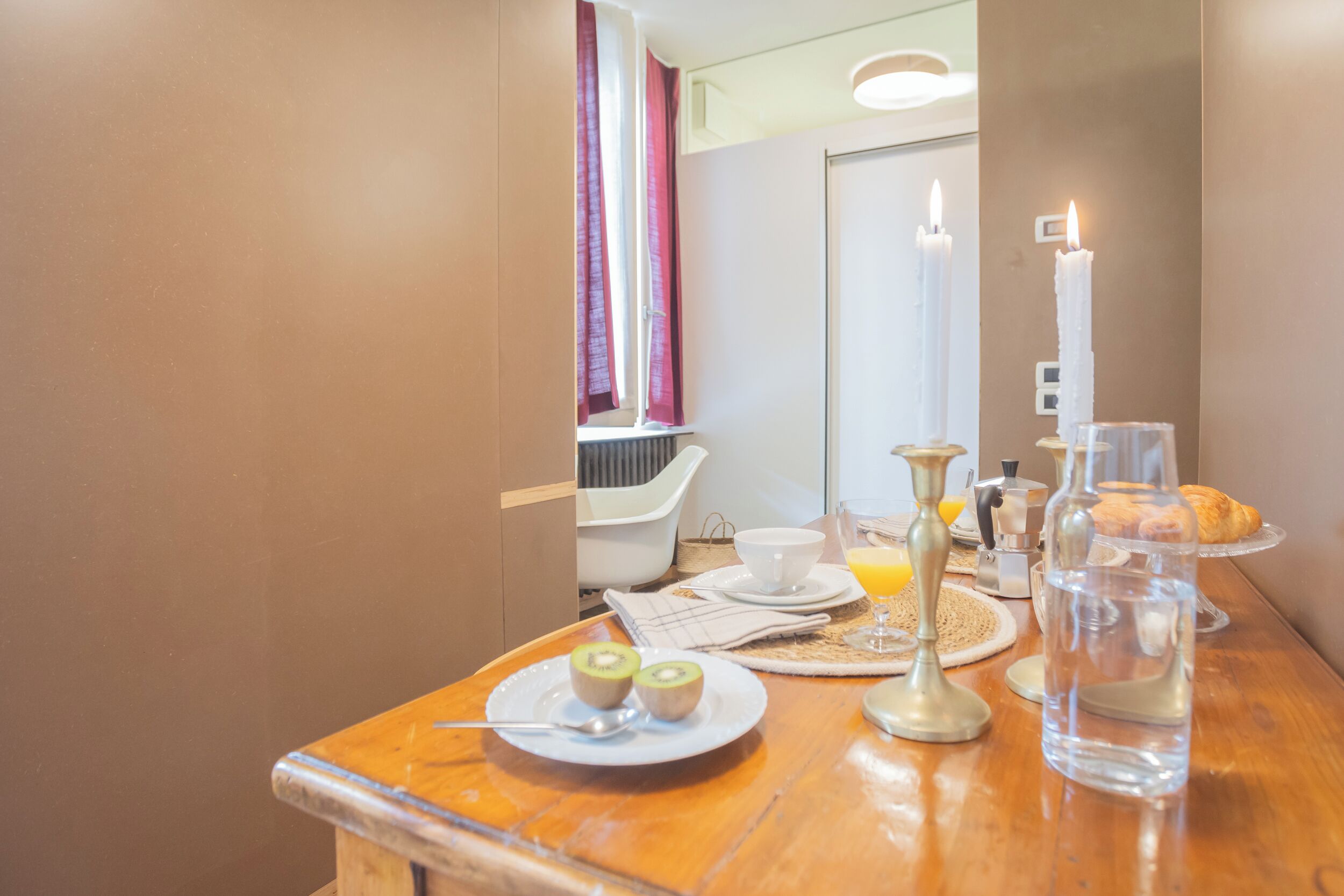 A breakfast table with a plate of kiwi slices, a glass of orange juice, a candle, and a bottle of water.