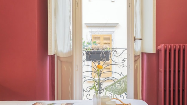 A hotel room with a bed, a table with a tray set, a window with curtains, and a radiator.