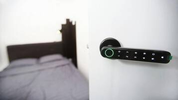 A bed with a headboard, a wall-mounted electronic device with a numeric keypad, and a door handle.