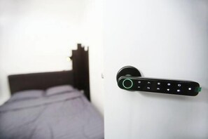 Una cama con cabecera, un dispositivo electrónico fijado a la pared con teclado numérico y un picaporte.