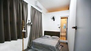 Een slaapkamer met een bed, gordijnen, een ventilator en een deur naar een badkamer.