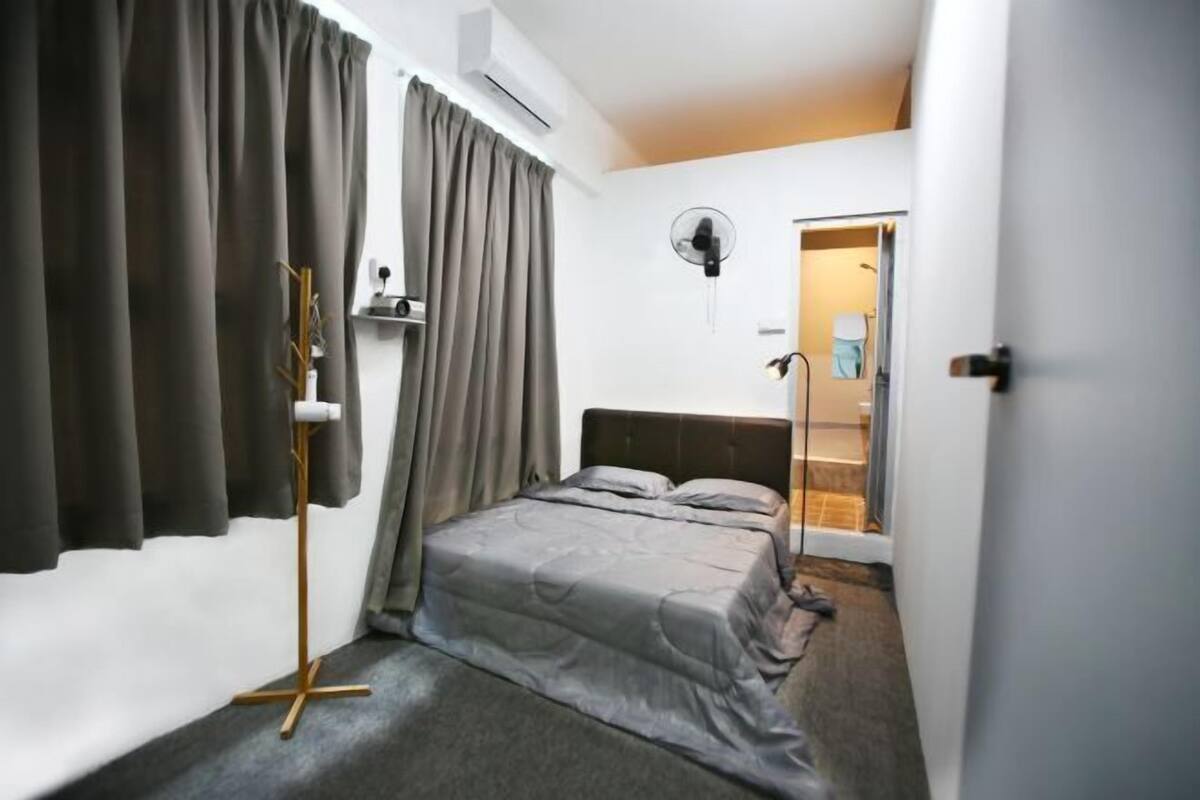 Quarto com cama, cortinas, um ventilador e uma porta que dá para um banheiro.
